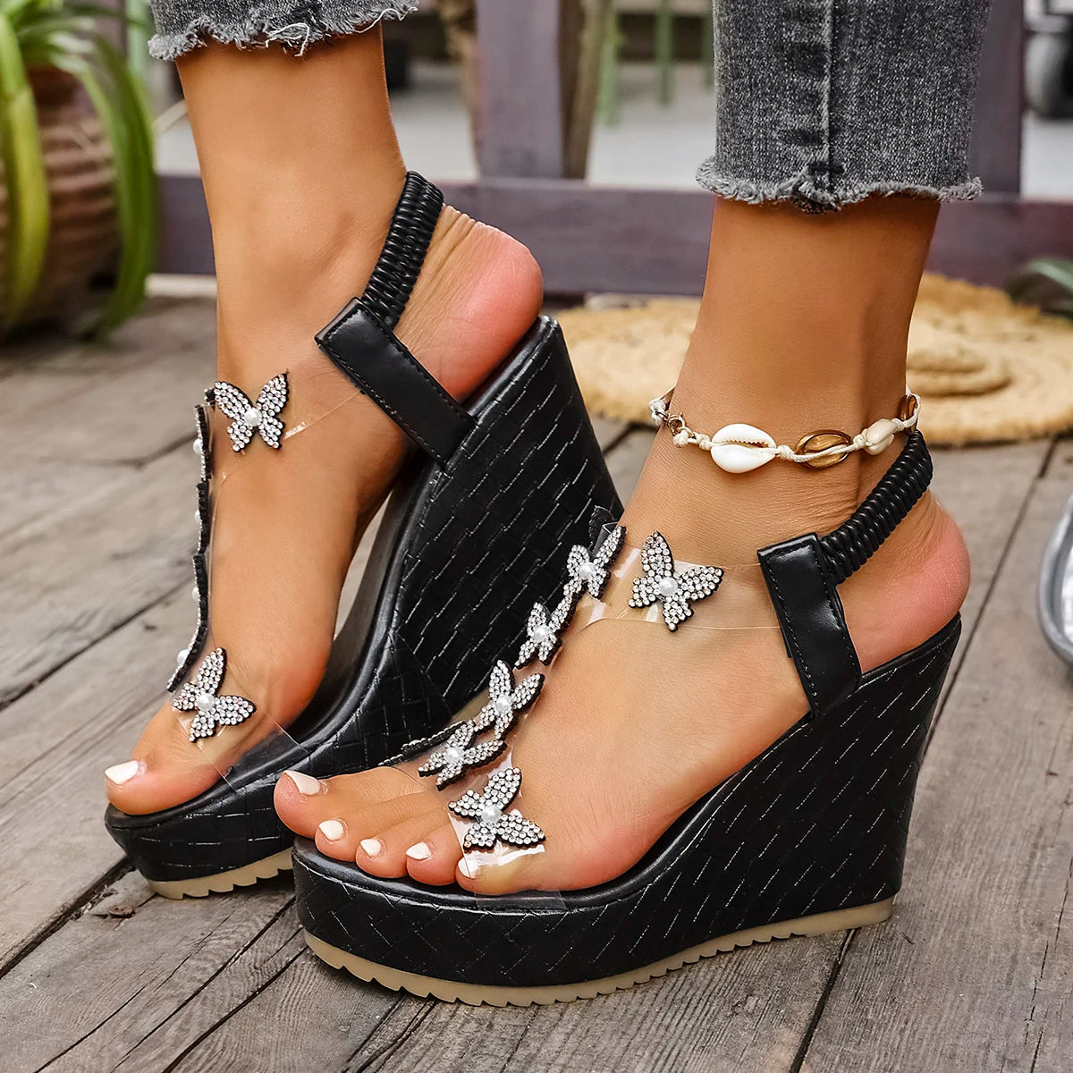 Black wedge sandals with butterfly embellishments on a wooden floor.