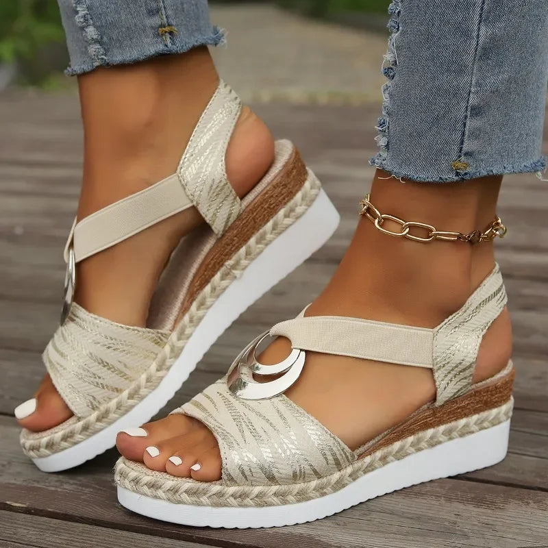 Beige espadrille sandals with wooden wedge sole worn with denim jeans on a wooden floor.