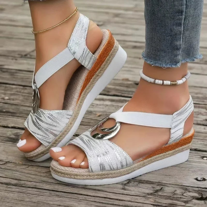 White wedge sandals with brown straps on a wooden floor