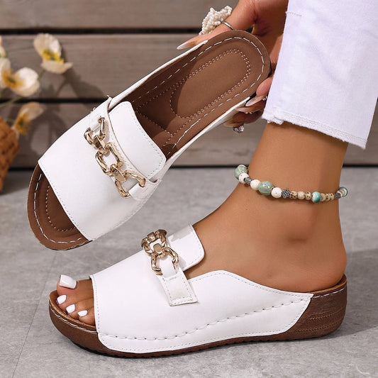 White sandals with brown soles worn by a person on a gray surface.